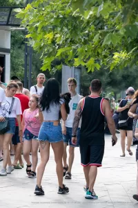 Фото тату на пояснице девушки, идущей по улице в компании людей. Видна татуировка в виде узора, выполненная в черных тонах.
