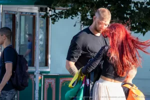 Мужчина с бородой обнимает девушку с рыжими волосами. На руке мужчины видна татуировка в стиле графики. Фото сделано на улице.