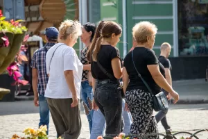 Фото женщины с татуировкой на шее, идущей по улице с двумя спутницами. Видна часть татуировки с загадочными символами.
