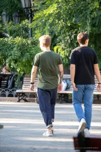 Фото тату: два мужчины идут по улице, у одного из них на плече видна татуировка в виде черного дракона.