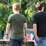 Фото тату: два мужчины идут по улице, у одного из них на плече видна татуировка в виде черного дракона.
