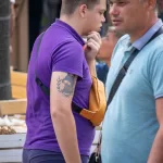 Фото тату котенка с веточками на плече. Черно-белый рисунок татуировки в реалистичном стиле, выполненный с высокой детализацией.