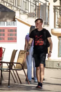 Фото тату на руке мужчины с арабской надписью и английским текстом 'Don't Shoot'. Уличная фотография, демонстрирующая современный стиль татуировки.