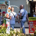 Фотография мужчины с татуировками на предплечьях, держащего букет белых цветов. Тату выполнены в черном цвете, с преобладанием геометрических и абстрактных мотивов.