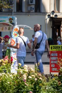 Фотография мужчины с татуировками на предплечьях, держащего букет белых цветов. Тату выполнены в черном цвете, с преобладанием геометрических и абстрактных мотивов.
