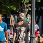 Фото тату на спине мужчины, идущего по улице. Видна часть татуировки с японскими иероглифами и изображением лица. Уникальный рисунок татуировки.