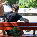 Крупный план татуировки на руке мужчины, изображающей японского карпа кои и волны. Фотография сделана на улице, мужчина сидит на скамейке.