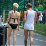 Фотография девушки и парня, идущих по улице. Видны татуировки на спине девушки и руке парня. Летний день, солнечная погода.
