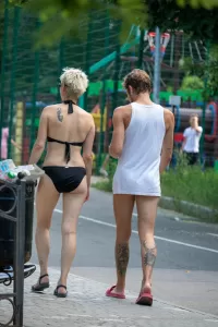 Фотография девушки и парня, идущих по улице. Видны татуировки на спине девушки и руке парня. Летний день, солнечная погода.