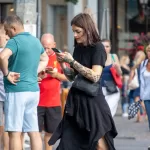 Фото тату на руках и шее девушки, смотрящей в телефон. Черно-белые татуировки в стиле графика, с детализированными узорами.