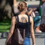 Фото тату: изображение головы льва в декоративной рамке на спине. Черно-серый рисунок татуировки с высокой детализацией и классическим дизайном.