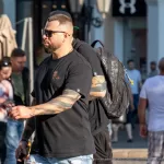 Фотография мужчины с татуировкой на руке, идущего по улице. Рукав татуировки в темных тонах, детализированные рисунки, уличный стиль. Фото тату.