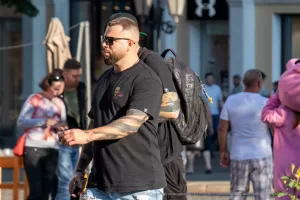 Фотография мужчины с татуировкой на руке, идущего по улице. Рукав татуировки в темных тонах, детализированные рисунки, уличный стиль. Фото тату.