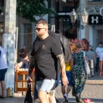Фотография мужчины с татуировкой на руке, идущего по улице. Рукав татуировки в темных тонах, детализированные рисунки, уличный стиль. Фото тату.