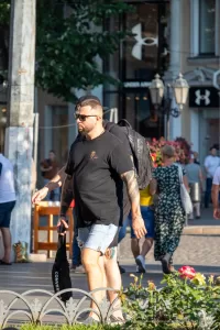 Фотография мужчины с татуировкой на руке, идущего по улице. Рукав татуировки в темных тонах, детализированные рисунки, уличный стиль. Фото тату.