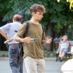 Фотография мужчины с татуировками на руке, держащего чашку кофе и идущего по улице.