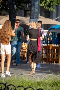 Фотография уличной татуировки на предплечье девушки, идущей по городской улице. Татуировка выполнена в темных тонах и выглядит стильно.