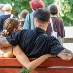 Фотография пары в объятиях, у мужчины татуировки на руке и шее, у женщины - на спине. Идеально для поиска идей для парных тату.