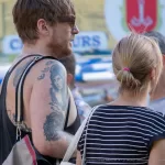Фото тату на плече мужчины: крупный план реалистичного портрета в черно-серых тонах, детализированный рисунок, уличная фотография.