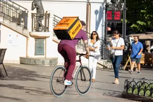 Фотография курьера на велосипеде с татуировкой на руке и оранжевой сумкой Raketa. Татуировка выполнена в темных тонах и изображает череп.