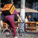 Фотография курьера на велосипеде с татуировкой на руке. Татуировка выполнена в темных тонах и изображает череп.