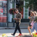 Фотография татуировки на руке мужчины, выполненной в темных тонах, на фоне городской улицы и рекламных плакатов.