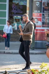 Фото татуировки на предплечье мужчины, выполненной в темных тонах, на фоне городской улицы и рекламных плакатов.