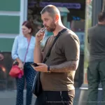 Фотография татуировки на руке мужчины, выполненной в темных тонах, на фоне городской улицы и рекламного щита.