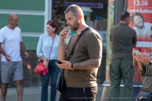 Фотография татуировки на руке мужчины, выполненной в темных тонах, на фоне городской улицы и рекламного щита.