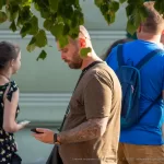 Фотография мужчины с татуировкой на руке, смотрящего в сторону. Татуировка выполнена в темных тонах и имеет сложный узор.