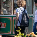 Фото мужчины с татуировкой на руке, стоящего на фоне киоска с напитками. Рисунок татуировки выполнен в темных тонах и включает в себя черепа и розы.