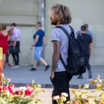 Фото мужчины с татуировкой на руке, идущего по улице. Рисунок татуировки выполнен в темных тонах и включает в себя черепа и розы.