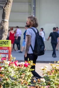 Фото мужчины с татуировкой на руке, идущего по улице. Рисунок татуировки выполнен в темных тонах и включает в себя черепа и розы.