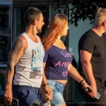 Фотография людей на улице с татуировками, идущих мимо кафе. Мужчина с татуировкой на руке и женщина в розовой футболке.