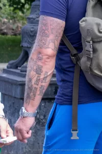 Фото тату на руке, выполненное в виде рукава. Изображены черепа, цветы и надпись на иностранном языке. Рукав татуировки выглядит детализированно и стильно.
