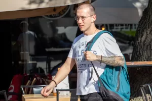 Фото тату: мужчина с татуировкой на руке, в наушниках и с рюкзаком. Детализированный рисунок татуировки с черепами и другими элементами.