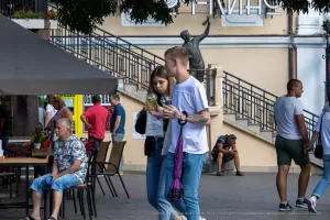 Фотография мужчины с татуировкой на предплечье, идущего по улице в окружении людей. Татуировка выполнена в реалистичном стиле с использованием ярких цветов.