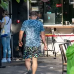 Фото тату на ноге и руке мужчины, идущего по улице. Вид сзади, татуировки в стиле графики и абстракции.