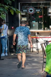 Фото тату на ноге и руке мужчины, идущего по улице. Вид сзади, татуировки в стиле графики и абстракции.