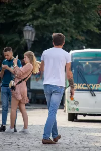 Фотография мужчины с татуировками на руках и спине, стоящего на улице. Современный стиль, городская обстановка, повседневная одежда. Детализированное фото тату.