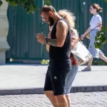 Фотография мужчины с татуировкой на руке, который увлеченно смотрит в свой мобильный телефон на улице.
