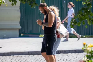 Фотография мужчины с татуировкой на руке, который увлеченно смотрит в свой мобильный телефон на улице.
