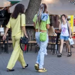Фотография девушки с татуировкой на плече, идущей по улице. Тату выполнено в черном цвете и сочетается с яркой одеждой.