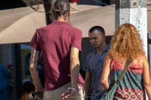 Фотография мужчины с татуировкой на руке, стоящего рядом с двумя другими людьми. Виден фрагмент татуировки на плече.