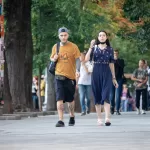 Фотография мужчины с татуировками на ногах, идущего по улице с девушкой. Татуировки выполнены в стиле графика и изображают черепа и растительные мотивы.