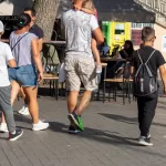 Фотография мужчины с татуировкой на ноге, идущего по улице. Татуировка выполнена в темных тонах и видна на икре.