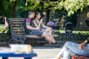 Фото тату: Молодой человек с татуировками на руках сидит на скамейке рядом с девушкой. Татуировки изображают яркие и красочные рисунки.