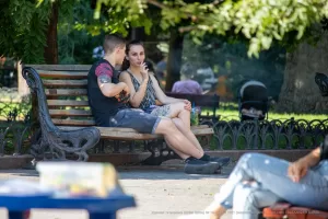 Фото тату на предплечье и ноге у пары, сидящей на парковой скамейке в солнечный день. Видны детали рисунков татуировок и общая атмосфера.