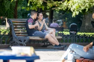 Фото тату: Молодой человек с татуировками на руках сидит на скамейке рядом с девушкой. Татуировки изображают яркие и красочные рисунки.