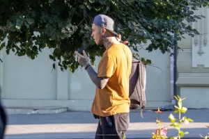 Фото тату на руках и шее мужчины, идущего по улице. Видны детализированные рисунки в стиле традишнл.